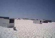 A group of beach huts on a white sand beach.