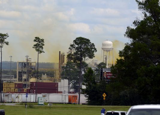 A yellow smoke billows from an oil refinery.