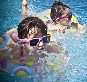 Two young girls wearing sunglasses in a swimming pool.