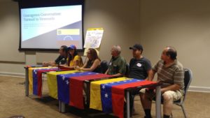 Venezuelan nationals sitting behind tables drapped with the Venezuelan flag