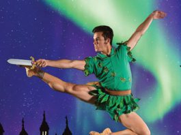 A male dancer in green jumps in front of a castle.