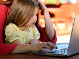little girl sitting on woman's lap using a laptop computer