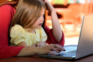 little girl sitting on woman's lap using a laptop computer