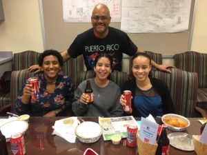 man wearing shirt that says "puerto rico" standing behind three teen girls seated at a table holding sodas