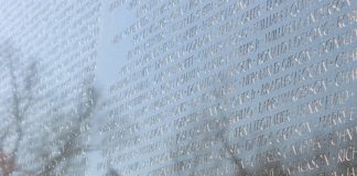 Names engraved into Vietname Memorial Wall with reflection of American flag