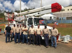 Nine employees of the electric company standing in front of a bucket truck