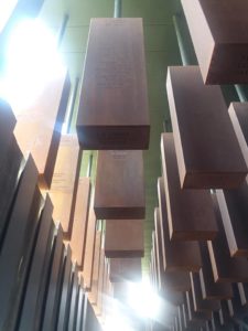 Large brick shaped memorial with names of poeple carved into them hanging from a ceiling