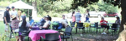 people sitting at small tables under a tree talking to each other