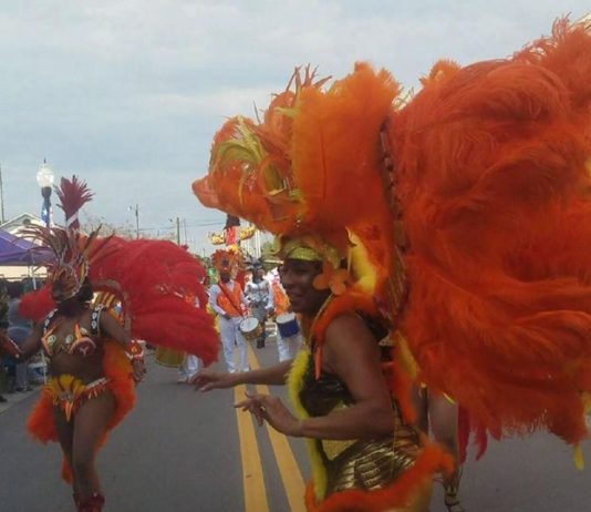 women dressed in with large orange feathers parading down a street