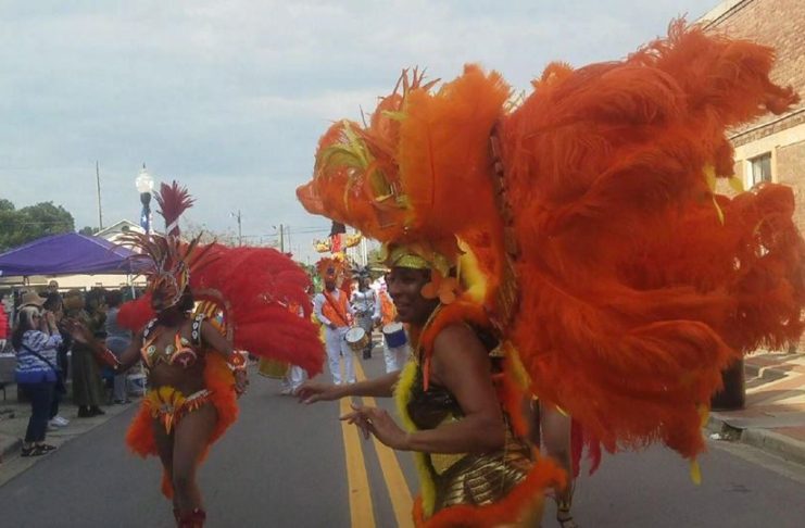 women dressed in with large orange feathers parading down a street