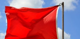 A red flag waving in the wind against a blue sky.