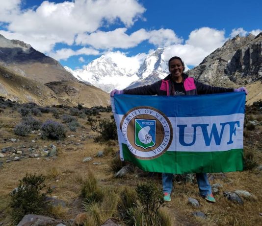 girl holding UWF flag on top of mountain