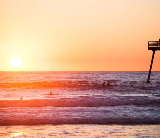 A group of surfers on the beach at sunset.