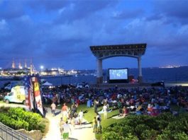 A group of people watching a movie on a lawn near the water.