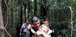 A man carrying a child through the woods.