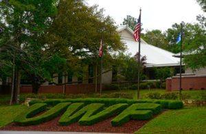 Letters UWF shaped hedges below three flagpoles.