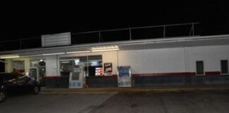 A car is parked in front of a gas station at night.