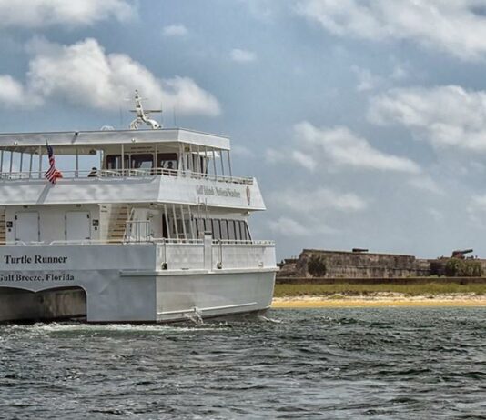 A white boat is traveling in the water near a small island.