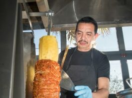 restaurant worker cutting meat and pineapple on from a vertical rotisserie