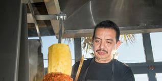 restaurant worker cutting meat and pineapple on from a vertical rotisserie