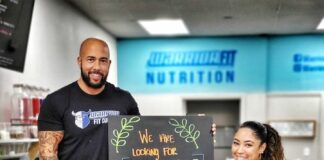 couple standing in front of counter and sign that says "warrior fit, we are looking for need coaches"