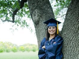 girl with graduation cap and gown standing against a tree