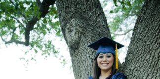 girl with graduation cap and gown standing against a tree