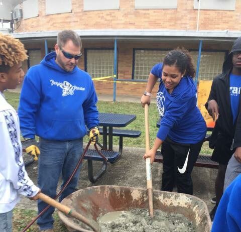 students are being taught how to mix cement in a wheelbarrow