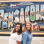 two women standing in front of a Pensacola mural