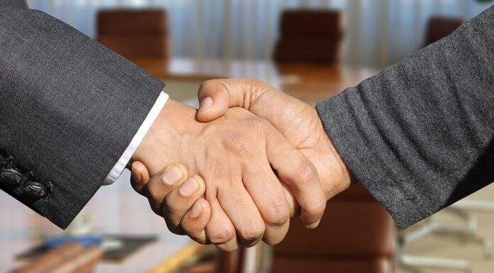 Two businessmen shaking hands in front of a conference room.