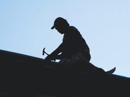 silhouette of roofer hammering on roof