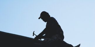 silhouette of roofer hammering on roof