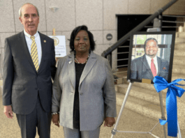 Mayor Sandy Stimpson and Jeanette Manzie standing by a photo of Councilman Manzie