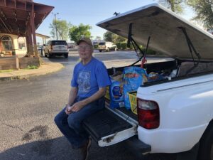 man sitting on truck tailgate next to cat food