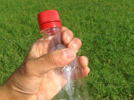 A person holding a plastic bottle in a grassy field.