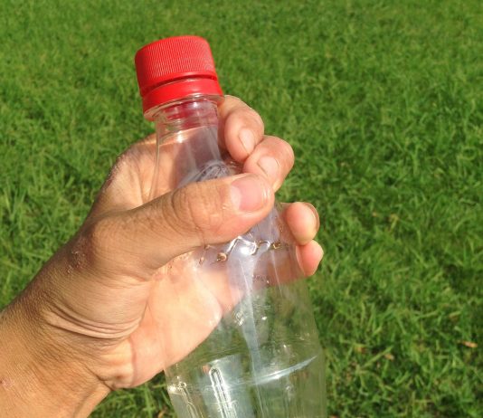 A person holding a plastic bottle in a grassy field.
