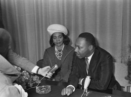Martin Luther King Jr speaking into a microphone with wife by his side.