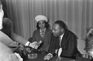 Martin Luther King Jr speaking into a microphone with wife by his side.