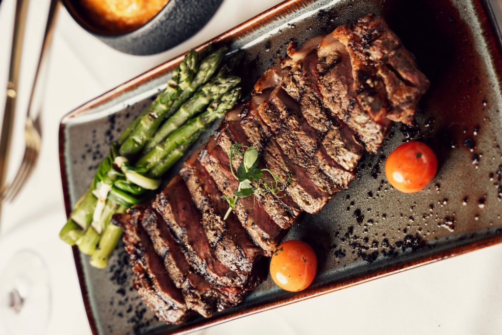 A delicious plate of Churrasco Steak, featuring with fresh asparagus and ripe tomatoes