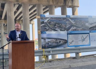 Speaker standing under a bridge at podium next to large photos of plans