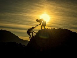 one person helping another climb a mountain