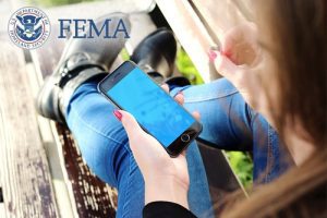 Cellphone in hand behind FEMA logo