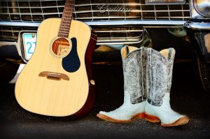 Guitar and cowboy boots leaning against a car grill