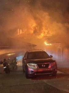 Car parked in front of a house that is in flames