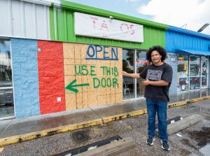 Owner of Tacos El Fluffy pointing at wood-covered windows where a vehicle crashed through.