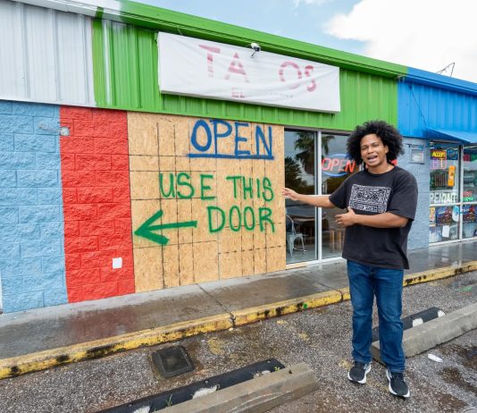 Owner of Tacos El Fluffy pointing at wood-covered windows where a vehicle crashed through.