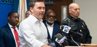 Pensacola Mayor D.C. Reeves speaking at a podium standing next to Pensacola Police Chief Eric Winstrom and city council members
