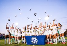 Female soccer league champions throw hats in the air while surrounding SEC trophy