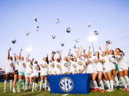 Female soccer league champions throw hats in the air while surrounding SEC trophy