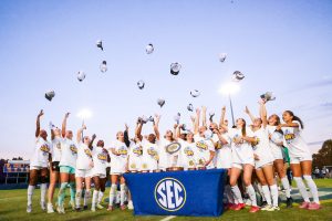 Female soccer league champions throw hats in the air while surrounding SEC trophy